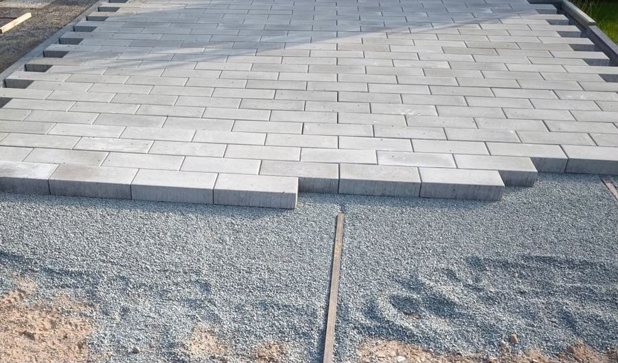 Frisch verlegte graue Betonpflastersteine im Reihenverband, davor das vorbereitete Splittbett mit Abziehlehre.