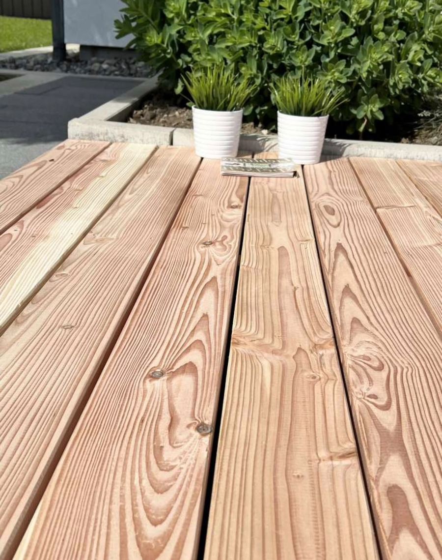 Neu verlegte Terrassendielen aus Lärchenholz mit gleichmäßigen Fugen, dahinter Pflanzkübel und Beeteinfassung.