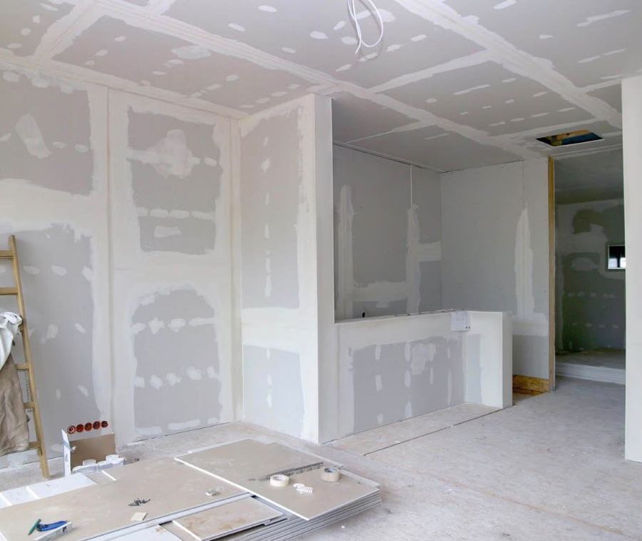 Fertig gestellte Trockenbauwände und abgehängte Decke mit verspachtelten Plattenstößen im Innenausbau, davor Gipskartonplatten und Werkzeug.