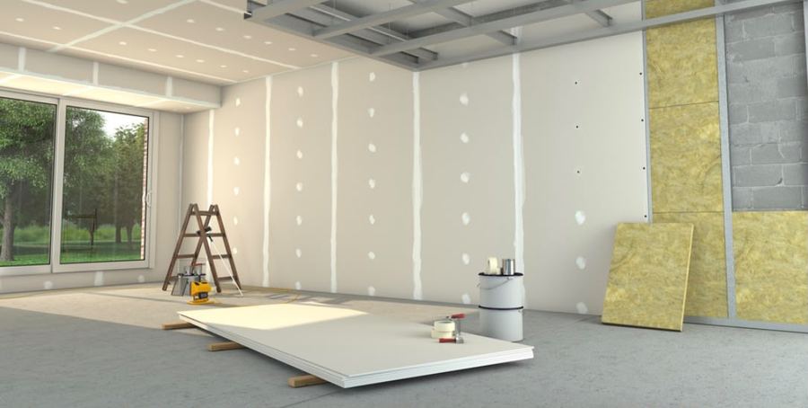 Trockenbauwand mit verspachtelten Fugen neben offener Ständerkonstruktion mit Mineralwolle-Dämmung, davor gestapelte Gipskartonplatten und Leiter.