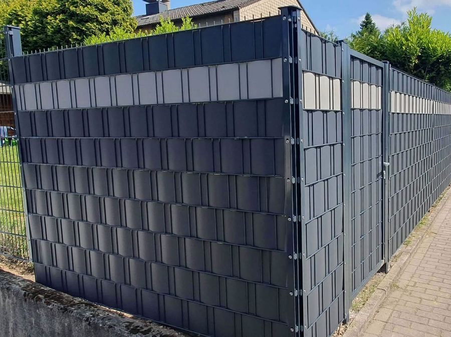 Fertig montierter Sichtschutzzaun mit Gartentor an der Grundstücksecke entlang eines gepflasterten Gehwegs.