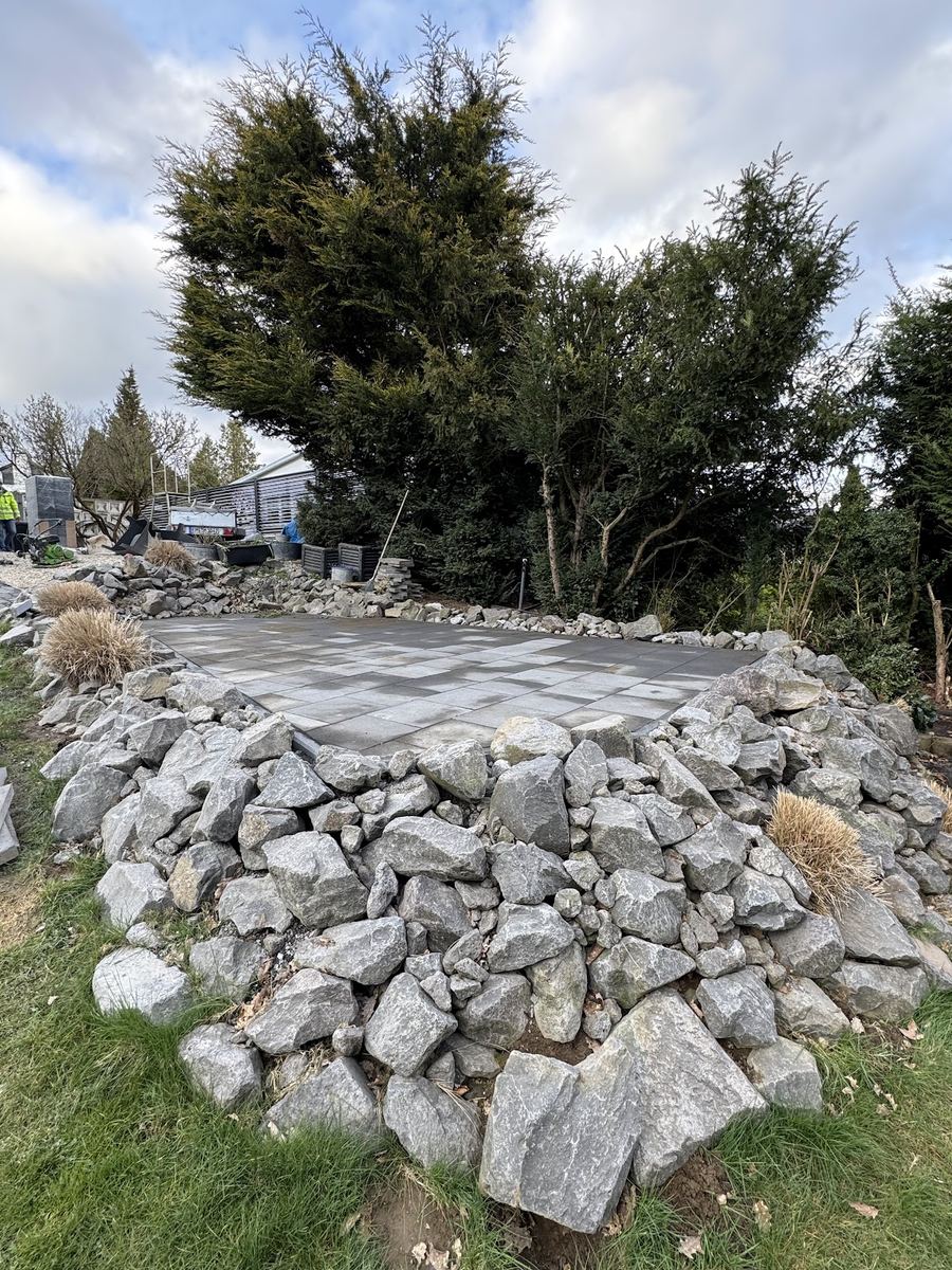 Fertige Plattenterrasse im Garten, ringsum mit Bruchsteinen als Steingarten eingefasst.