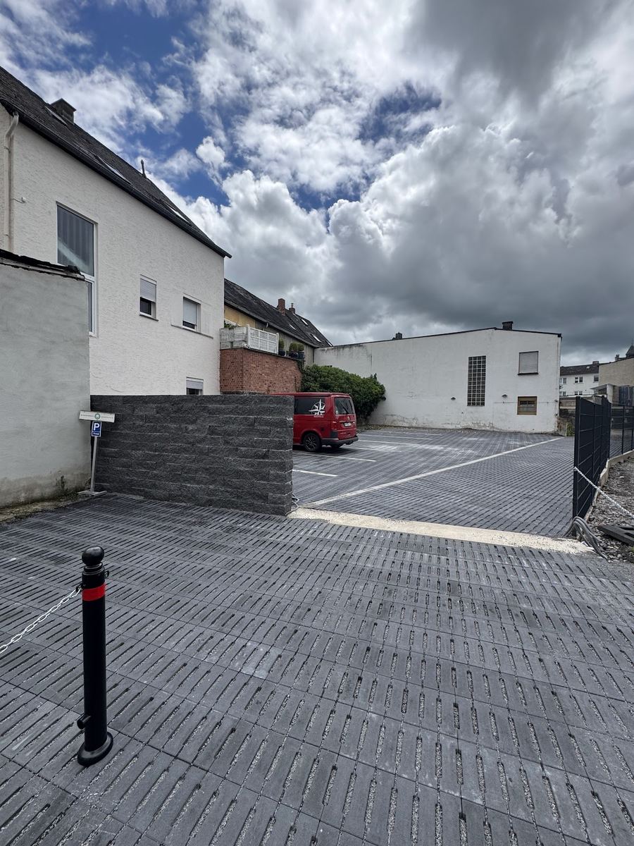 Neu gepflasterter Parkplatz mit Rasenfugensteinen und dunkler Natursteinmauer.