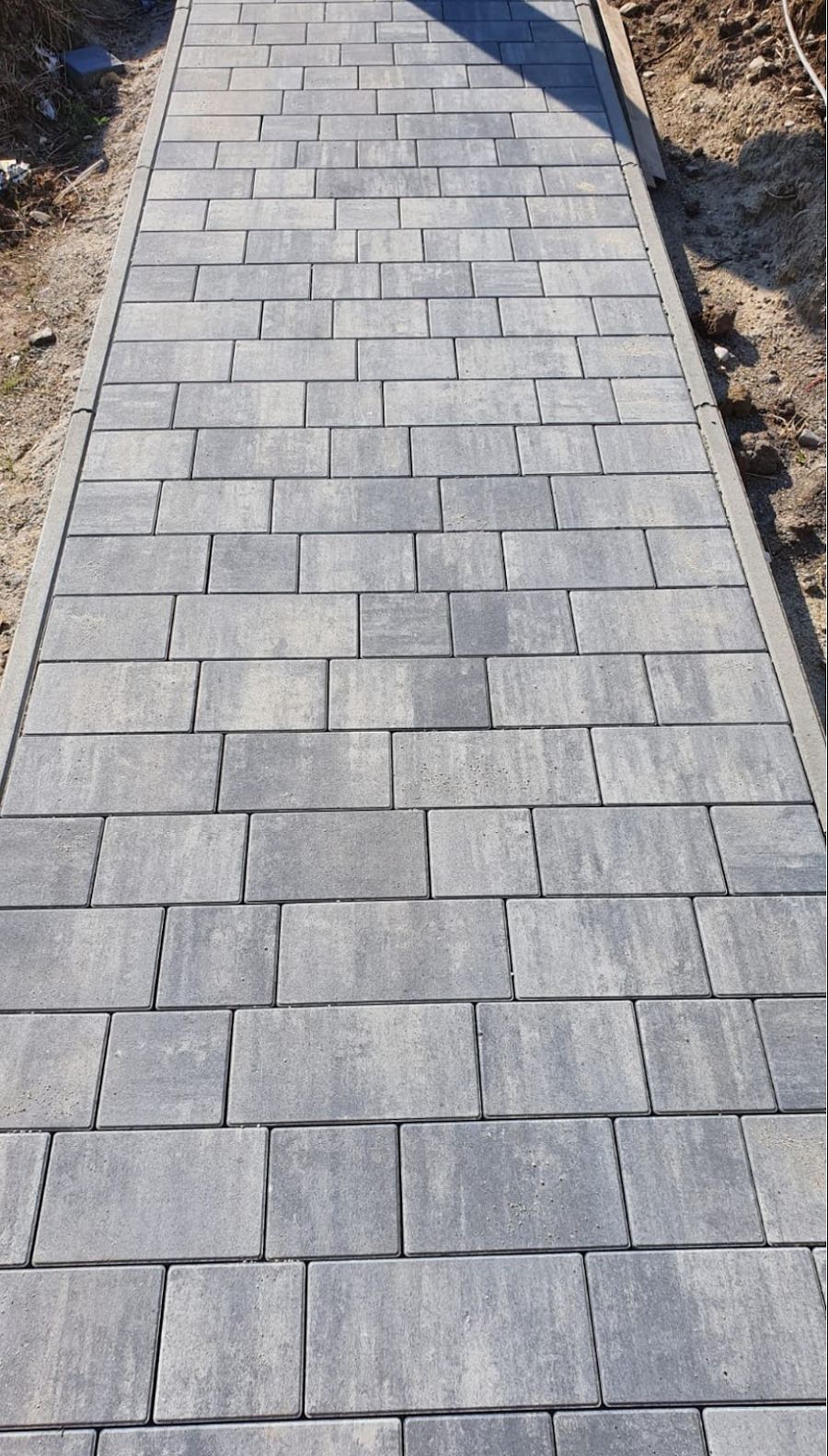 Frisch verlegter grauer Pflasterweg mit Randsteinen in verschiedenen Formatgrößen.