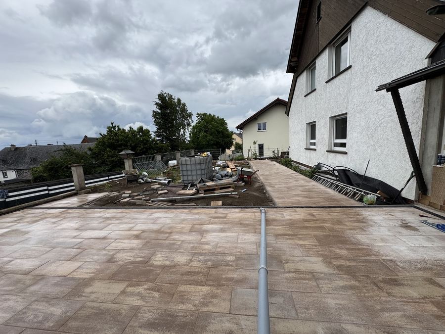 Frisch verlegte großformatige Terrassenplatten am Haus, im Hintergrund noch Baustellenmaterial.